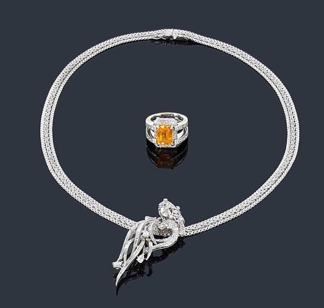 Motif en or gris 18K (750 ?) et platine représentant le signe du verseau serti de diamants de taille brillant, calibrés et navettes, monté sur un collier tissé d'or gris 18K (750 ?). 
Hauteur du motif: 6 cm - Longueur du collier: 45,5 cm environ. Poids brut: 42,7 g