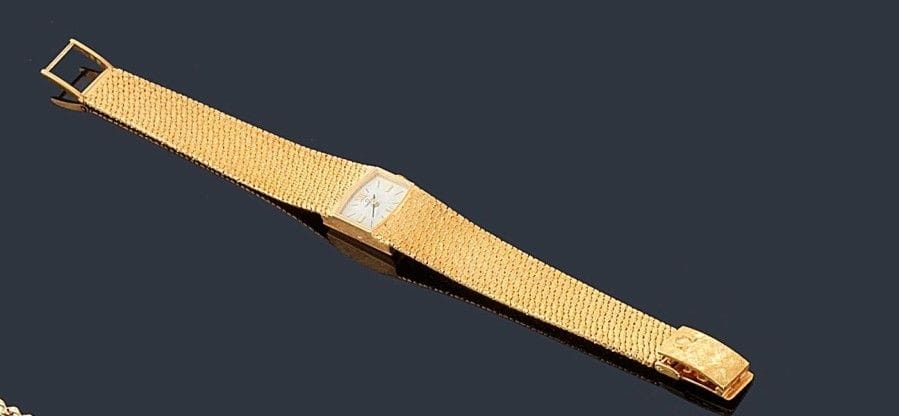 OMEGA
Montre de dame en or jaune 18K (750 ?), cadran oblong, fond blanc, index bâtons, bracelet ruban en or jaune 18K (750 ?) satiné à l'imitation du lamé, mouvement mécanique. 
Longueur: 16,5 cm environ. Poids brut: 43,4 g (mouvement à réviser)