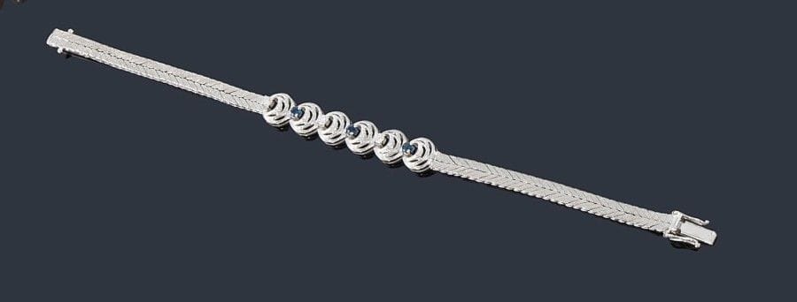 Bracelet en tresse d'or gris 18K (750 ?) satiné, orné de 3 diamants alternés de trois saphirs. 
Longueur: 18,5 cm environ. Poids brut: 23,2 g