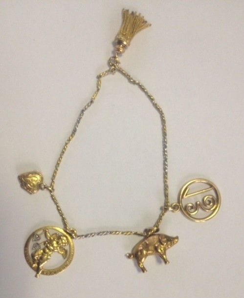 Bracelet en or jaune 18K (750 ?), retenant en pampilles: un pompon en or 18K (750 ?) terminé de floches, un petit cochon 18K (750 ?), une médaille porte-bonheur (14K), un médaillon ouvrant en forme de coeur 18K (750 ?) et une médaille ornée d'un cupidon. 
Poids brut: 16,9 g