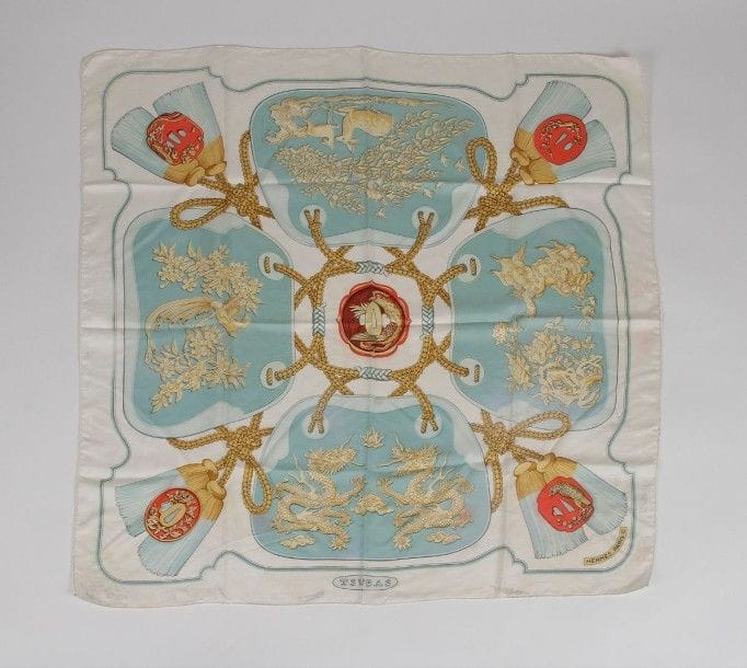 2 Carrés Hermès:
«Vue du carrosse La galère La Réale», fond crème, entourage vert (taches).
«Tsubas», fond blanc, motifs bleu clair. 
(taches).