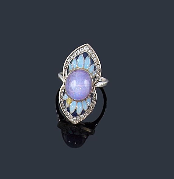 PAUL FOLLOT
Bague en platine formant une navette resserrée, centrée d'un saphir cabochon astérié épaulé de pétales émaillés blanc sur fond bleu, la bordure ourlée de diamants. Tour de doigt: 56. Poids brut: 11,6 g (manque). 
Paul-Frédéric Follot (1877-1941), créateur polymorphe, est avant tout dessinateur et décorateur. Il créé en 1905 des bijoux qu'il présente aux Salons de la Société des artistes français. Il met en scène à ces occasions, du mobilier, des objets d'art et des bijoux qu'il a lui-même élaborés. Son travail se caractérise à cette époque par des créations «naturalistes» où les bijoux forment des fleurs, des insectes. La bague que nous présentons peut donc être datée de cette période. Voir par exemple A. Duncan (The Paris Salons 1895-1914, Jewellery I: The designers A-K, 1994, 
p. 242-245) pour des modèles de bijoux émaillés.