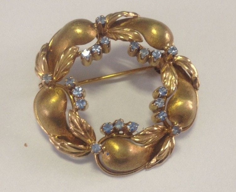 Broche en or jaune 18K (750 ?) formant une couronne de fruits et feuilles, piquée de pâtes de verre bleues. 
Diamètre: 3,5 cm environ. Poids brut: 11,1 g