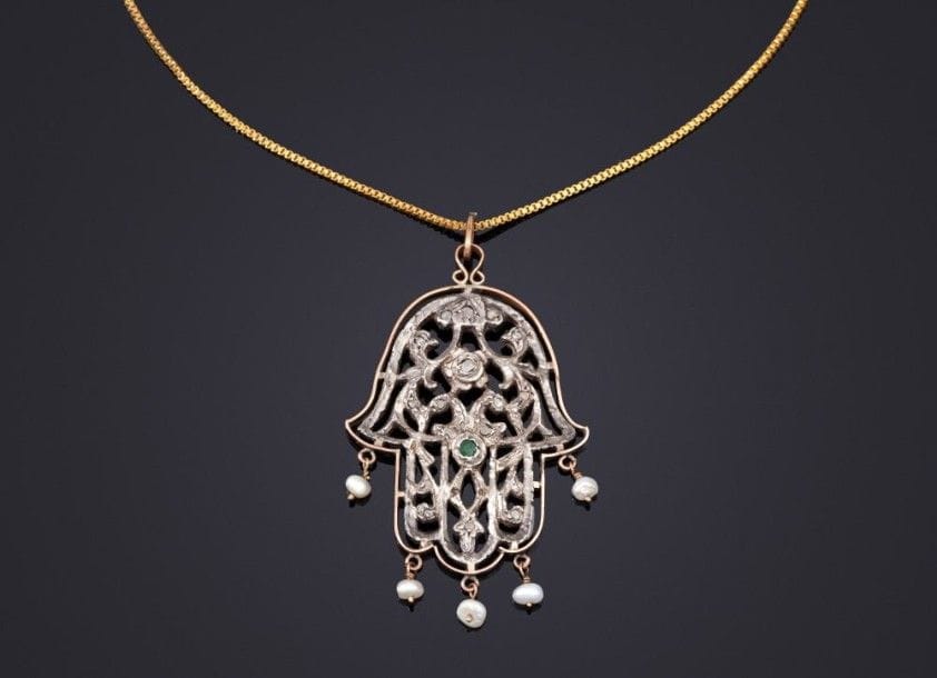 Pendentif en khamsa en argent souligné d'or, Tunisie, XXe siècle
Pendentif en khamsa en argent ajouré de palmettes, bordé d'or et serti de cabochons en diamants et émeraudes, à pendeloques de petites perles. Revers doré. Petite chaîne en métal doré.
Dim.: 6,3 x 3,7 cm.
Pour un exemple similaire, voir S. Gargouri - Sethom, Les Bijoux de Tunisie, Dunes Editions, 2005, p. 141.
Necklace with a gold and silver khasma pendant, Tunisia, Tunis, 20th century