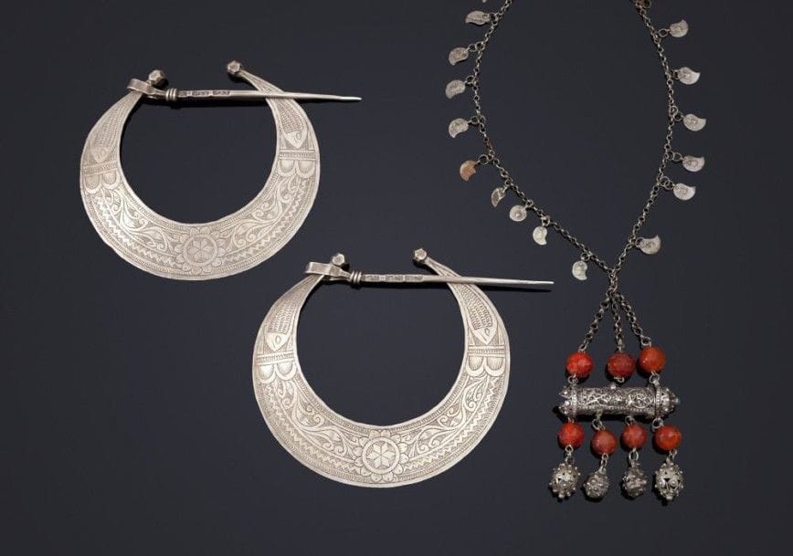Paire de fibules, hillal, en argent, Tunisie, et collier, qannuta, Algérie, fin XIXe siècle
Croissant de lune ou hillal, à décor incisé d'une rosette centrale entourée d'arabesques végétales et de poissons aux extrémités; et chaîne en argent retenant un porte - talismanique tubulaire à pampille de perles facettées en agate.
Diam.: 13,9 cm.
PB: 196 g avec poinçons tunisiens.
Long.: 41,5 cm.
PB: 81g.
Voir pour d'autres exemples Clémence Sugier, Symboles et bijoux traditionnels de Tunisie, Céres Productions, 1969, p. 42; Samira Gargouri - Sethom, Les Bijoux de Tunisie, Dunes éditions, 2005, p. 94.
Pair of silver fibulaes, Hillal, and a qannuta, necklace, Tunisia and Algeria, late 19th century.