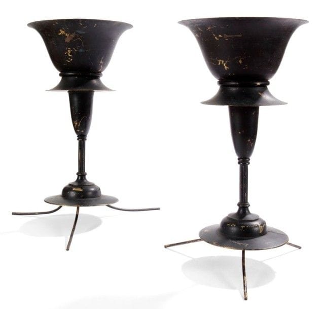 ARTS and CRAFTS

Paire de lampes en laiton postérieurement laquées noir.
Les bases circulaires reposent sur trois pattes (permettant la suspension ?) et reçoivent un fût cannelé surmonté d'un diabolo asymétrique formant vasque lumineuse. 
Les intérieurs des parties recevant l'éclairage, laqués blanc postérieurement, présentent trois languettes qui maintenaient probablement un disque de verre (manquant).
Hauteur: 47 cm