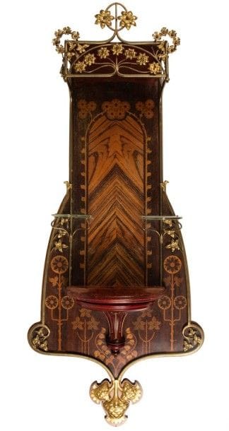 STILE LIBERTY (Art nouveau italien)

Haute étagère murale de collectionneur à trois tablettes.
Le décor de marguerites et de fleurs d'ornement, exécuté en marqueterie de bois précieux sur fond de palissandre, est décliné en métal doré sur le fronton et sur le jonc appliqué en pourtour.
La partie basse reçoit un décor de chardons réalisé en métal repoussé et doré.
L'étagère centrale en acajou nervuré et mouluré reprenant en sculpture le thème décoratif floral, les deux étagères supérieures au plateau en verre soutenu par des jambages en métal doré.
Hauteur: 120 cm