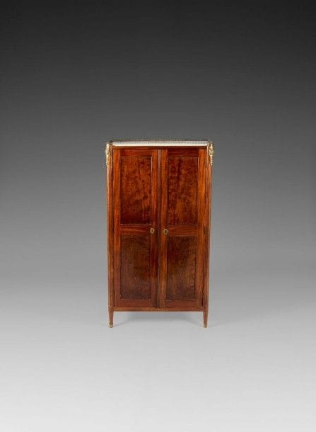 Armoire en acajou mouluré ouvrant à deux portes, les montants arrondis à cannelures reposant sur de petits pieds fuselés; dessus de marbre blanc à galerie.
Époque Louis XVI.
H.: 146,5 cm, L.: 80 cm, P.: 37 cm