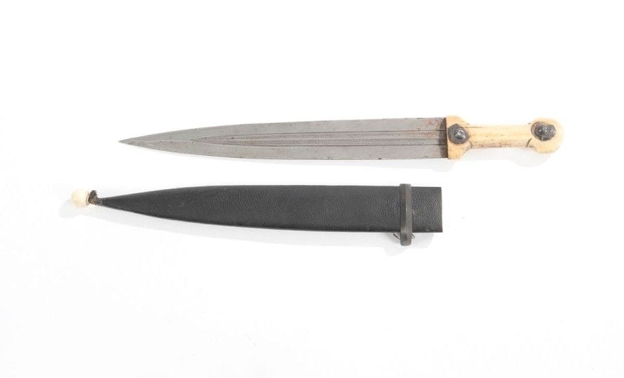 Kindjal. Garde en os à boutons acier. Lame à deux pans creux travaillés en Damas. Fourreau cuir et bois à une garniture acier. Boule en os à l’extrémité.  Long. 48,5 cm

