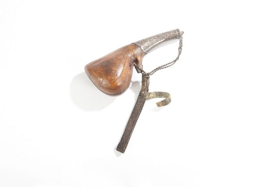 Poire à poudre. En peau de sexe de chameau décorée, embout en argent ouvragé et niellé, avec chainette et courroie d’attache.  Long. 22,5 cm


