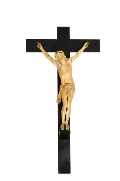 Grand Christ en ivoire sculpté. Tête inclinée sur l'épaule droite, ceinte d'une couronne d'épines torsadée, chevelure tombant en mèches ondulées sur les épaules, yeux levés vers le ciel, bouche ouverte avec dentition, périzonium retenu par une cordelette avec chute latérale sur la hanche droite, jambes et pieds parallèles reposant sur un suppedanum. Belle qualité d'exécution avec réseau veineux sur les bras et le cou accentuant le réalisme.
XVIIe siècle.
Sur une croix en bois noirci.
Christ H.: 58 cm; H. totale: 98 cm; L.: 49,7 cm
Un doigt recollé de la main gauche