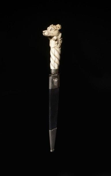 Couteau de vénerie 
Longue poignée torsadée en ivoire, à pommeau sculpté en ronde-bosse d'une tête de chien (fêlure). Monture nickelée, garde à deux quillons. Lame à dos plat, contre tranchant et pans creux. 
Fourreau en cuir noir à deux garnitures découpées, nickelées. 
B.E. XXe siècle. 
L.: 43,5 cm
