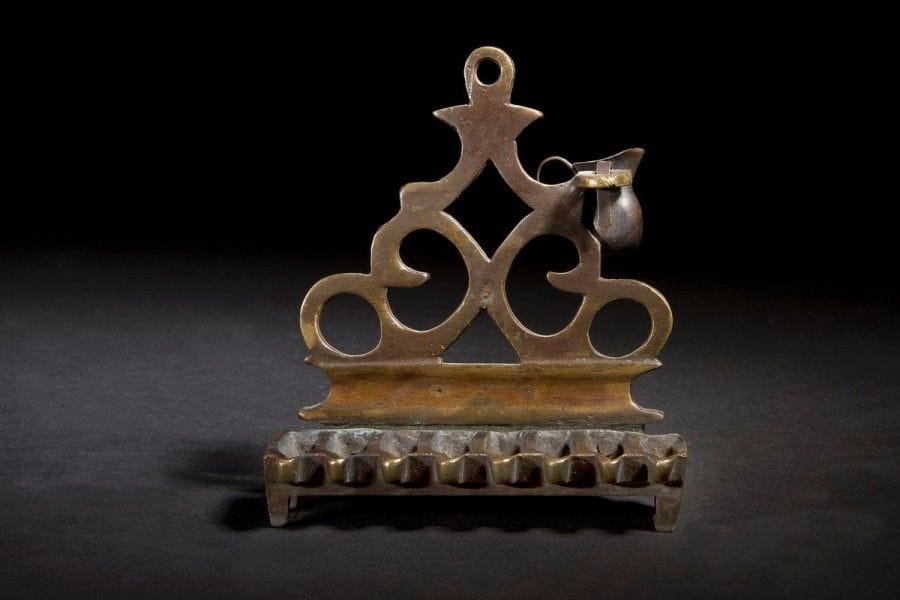 LAMPE DE HANOUCCA 
Bronze fondu et ajouré. 
Pologne, XVIIe ou XIXe siècle. 
Hauteur : 12,2 cm 
Le shamash manque. Sur la droite, une petite jarre à huile qui n’est pas d’origine a été ajoutée. Modèle de style XVIIIe siècle mais pouvant être postérieur. Mots clés : judaica, jewish, hebreu, hebrew, rabbin, synagogue, juif, juive, israélite, hebraica, judaism, torah, juden, sionism