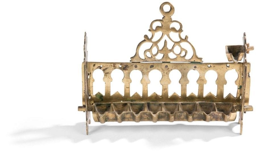 LAMPE DE HANOUCCA 
Bronze ajouré. 
Afrique du Nord, XVIIIe ou XIXe siècle. 
Dosseret à mihrabs surmonté d’un fronton triangulaire. 
Complète de son shamash et de ses contreforts. Bel exemplaire. 
18,5 x 26 cm Mots clés : judaica, jewish, hebreu, hebrew, rabbin, synagogue, juif, juive, israélite, hebraica, judaism, torah, juden, sionism
