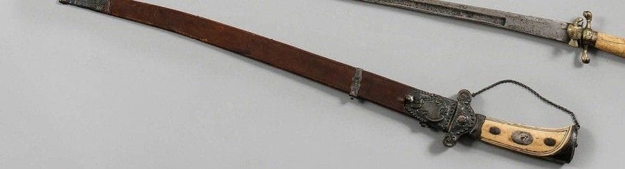 Beau couteau de vénerie.
Poignée en ivoire à trois boutons de rivure. Garde à chainette et monture en argent. Lame à dos plat et pans creux. Fourreau en cuir à trois garnitures en argent travaillé en suite.
B.E. Vers 1760-1780.