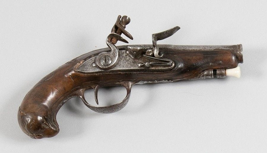 Pistolet de voyage à silex.
Canon rond, à pans au tonnerre. Platine et chien col de cygne, à corps plat, gravé de rinceaux et d'un cerf. Monture et crosse en noyer sculpté d'une tête d'oiseau avec incrustations d'argent.
B.E.
