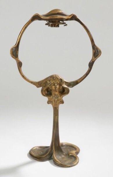 TRAVAIL ART NOUVEAU dans le goût de MÉLIODON

Pied de lampe de salon. Épreuve en bronze, partiellement doré, à décor d’une tête de jeune fille. Base trilobée rappelant un trèfle pouvant former vide-poche.
H.: 47,5 cm