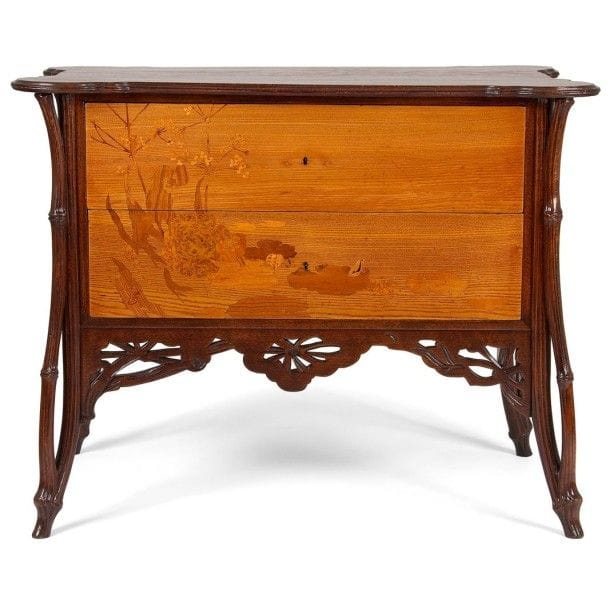 Émile GALLÉ (1846-1904)

La Berce des près, circa 1902/04
Rare commode, dite Sauteuse à deux tiroirs sans traverse, en placage de frêne et en hêtre sculpté et teinté. Le corps suspendu reçoit les deux tiroirs au décor en façade, de Berces des près bordant un marais présentant des nénuphars et animé d’une grenouille, réalisé en marqueterie de bois précieux et indigènes. La ceinture ajourée et sculptée reprend le thème décoratif des ombellifères. Les quatre jambages d’angle sont traités et sculptés dans le goût arborescent. Le dessus est constitué d’un plateau chantourné en débordement. Le dos panneauté est exécuté en noyer. État et restaurations d’usage, partie centrale de la ceinture ajourée non d’origine.
Signée GALLÉ en lettres japonisantes verticales dans le décor en marqueterie. 84 x 107 x 63 cm (Biblio. Gallé Furniture - Alastair Duncan et Georges de Bartha. Éditions Antique Collectors’ Club, Woodbridge, Suffolk, U.K., 2012. Le dessin préparatoire et le calque d’exécution du décor en marqueterie de ce modèle de commode, deux documents conservés au Musée d’Orsay, sont reproduits page 330 - Important: De la série de mobilier La Berce des près par Émile Gallé, seul ce modèle de commode a échappé à toute iconographie éditée, ancienne ou moderne. N’ont été publiés, jusqu’à aujourd’hui, que les dessins préparatoires du meuble, de certains de ses détails ainsi que le calque d’exécution du décor en marqueterie, l’ensemble de ces documents étant conservé au Musée d’Orsay)