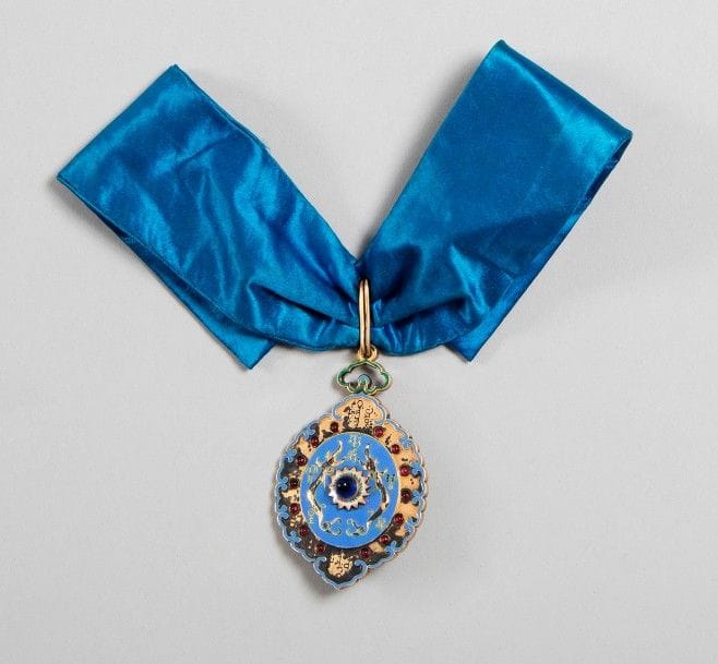 CHINE 
ORDRE DU DOUBLE DRAGON, crée en 1881. 
Rare insigne avant 1900. 
En vermeil, émaillé à l’avers, orné de perles en verre rouge sur le pourtour et au centre d’un cabochon en verre bleu. 
Décoré à l’avers de deux dragons et d’idéogrammes. Revers décoré en suite. 
Belle cravate en soie bleue. 
Ht : 7 x 5 cm - Poids brut : 70 g
T.T.B.