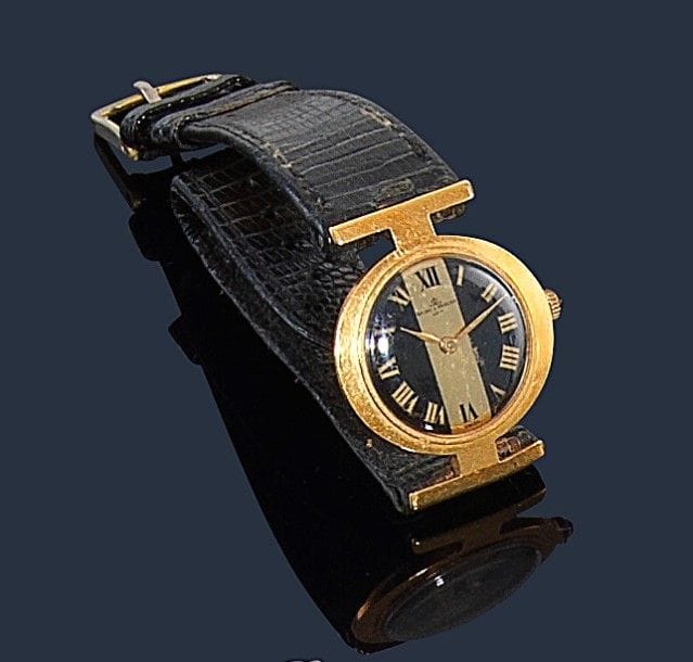 BAUME & MERCIER.
Montre de dame en or jaune 18K (750‰), le cadran formant avec les anses un Phi, fond noir, index chiffres romains, bracelet cuir boucle métal, mouvement mécanique. Numérotée 354145 36618. 
Poids brut : 24,2 g