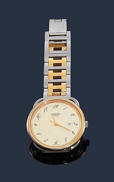 HERMES.
Montre pour homme modèle Arceau en acier et métal doré, boîtier rond, fond crème, index chiffres arabes, guichet dateur à 3h, bracelet articulé de H imbriqués, mouvement quartz. Signée et numérotée 164186. 
Diamètre : 28 mm 
Dans son écrin. 