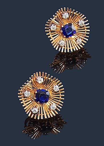 Paire de clips d’oreilles en fils d’or jaune 18K (750‰) à décor rayonnant, ornés chacun d’un saphir, piqués de diamants de taille ancienne. 
Travail français des années 50. 
Diamètre : 2,5 cm environ. 
Poids brut : 16,9 g