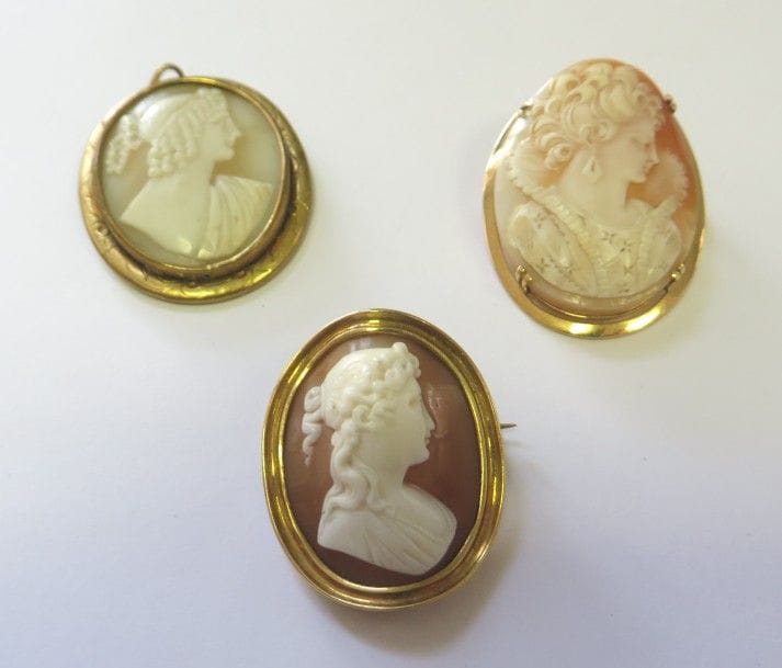 Lot de deux broches en or jaune 18K (750‰), chacune ornée d’un camée coquille sculpté du portrait d’une jeune femme de profil. Poids brut : 21,4 g. On joint un pendentif en métal orné d’un camée coquille sculpté d’une jeune femme de profil. 