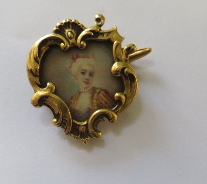 Broche en or jaune 18K (750‰), ornée d’une miniature sur ivoire représentant une jeune femme dans le goût du XVIIIe siècle. Numérotée 1552. Dimensions : 2,8 x 3,2 cm environ. Poids brut : 9,2 g