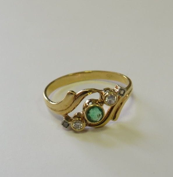 Bague en or jaune 18K (750‰), ornée d’une émeraude sertie clos épaulée de petits diamants et de roses. 
Tour de doigt : 53. Poids brut : 2,2 g