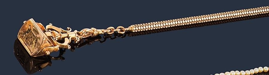 Chaîne giletière en or jaune 18K (750‰) retenant un cachet gravé d’armoiries sur deux faces, la troisième chiffrée. Travail français. Poids : 68,3 g