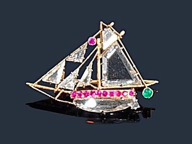 Broche en or jaune 18K (750‰) en forme de voilier, les voiles et la coque sertis de diamants taillés en table, agrémentée de petits rubis et d’une émeraude. 
Dimensions : 2,5 x 1,7 cm environ. 
Poids brut : 2,6 g