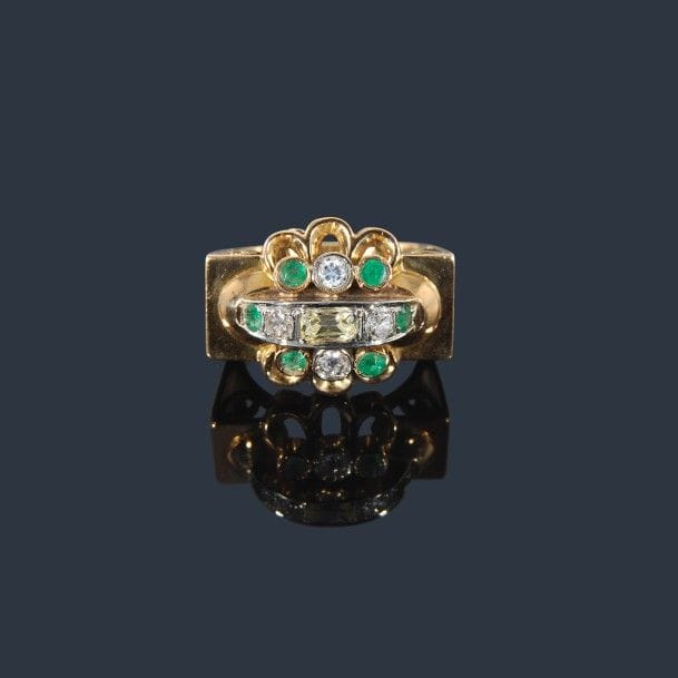 Bague en or jaune 18K (750‰), ornée d’une ligne de diamants de taille ancienne épaulée d’émeraudes, entre deux lignes d’émeraudes et de diamants alternés, la composition soulignée d’arcatures. Travail des années 1950. Tour de doigt : 54/55. 
Poids brut : 12,3 g 
(chocs, égrisures)