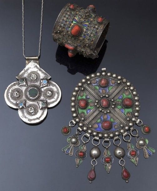 Collier, foulet khamsa, en argent, Maroc, Anti-Atlas, Vallée du Draa, XXe siècle
Pendant foulet khamsa quadrilobé en argent plané à décor repoussé de petites perles entourant des cabochons de verre verts et pierres turquoises. Poinçon et chaîne en argent. 
Long. pendant : 11,2 cm
Pb : 78 g.
État : infimes éclats sur cabochons, petites rayures. 
A necklace with a silver amulet, foulet khamsa, Morocco, Anti Atlas, Draa Valley, 20th century 