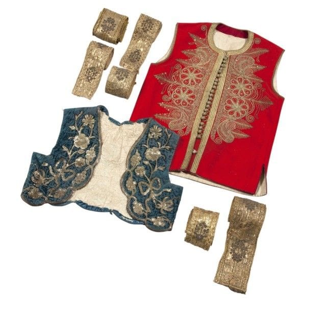 Boléro et gilet, Turquie ottomane, vers 1920-1930 
Boléro sans manches de velours bleu vert, brodé de fils métalliques dorés de tiges de roses et d’œillets aux points de chaînette, doublure de coton beige ;-gilet sans manche de feutre rouge brodé de fils métalliques de rosaces, de boteh et de tiges végétales. Joints neuf galons brochés de fils métalliques dorés. 
Dim. boléro : 27 x 33 cm ; gilet : 49 x 33 cm ; galons : entre 91 et 106 cm 
État : boléro : velours passé 
An Ottoman bolero and a jacket, Turkey, circa 1920-30
