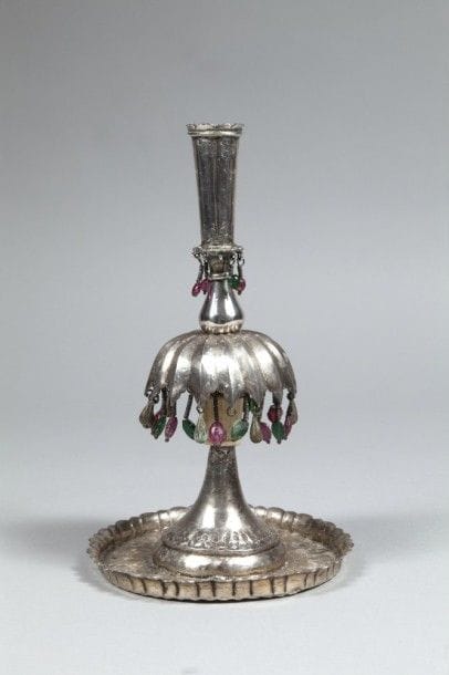 Bougeoir à pampilles, Proche-Orient, XXe siècle
Bougeoir en métal argenté ciselé à partie centrale cannelée à pampilles de métal et de perles de verre rose et vert, reposant sur une base circulaire. Partie du piédouche en os.
H. : 25,2 cm ; diam. : 14,5 cm
État : manques de pampilles. 
A silver plate candlestick, Near East, 20th century