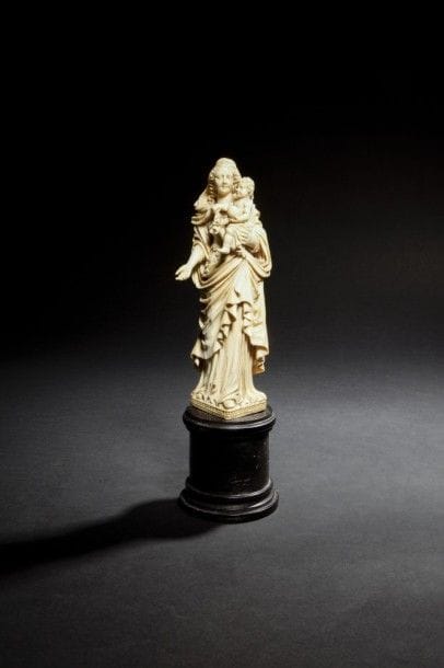 Vierge à l’Enfant en ivoire sculpté en ronde-bosse. Debout, elle porte l’Enfant nu sur son bras gauche ; elle est coiffée d’un voile dont l’Enfant tient un pan dans sa main droite ; elle est revêtue d’une robe avec justaucorps festonné et d’un manteau qui revient sur le devant en formant de nombreux plis arrondis et des ondulations sur les bords ; terrasse ornée de deux rangs de perles..
Pays-Bas ?, XVIIe siècle.
Hauteur : 19,5 cm - Hauteur totale : 27,5 cm.
Soclée.
(avant-bras droit de la Vierge refait).

