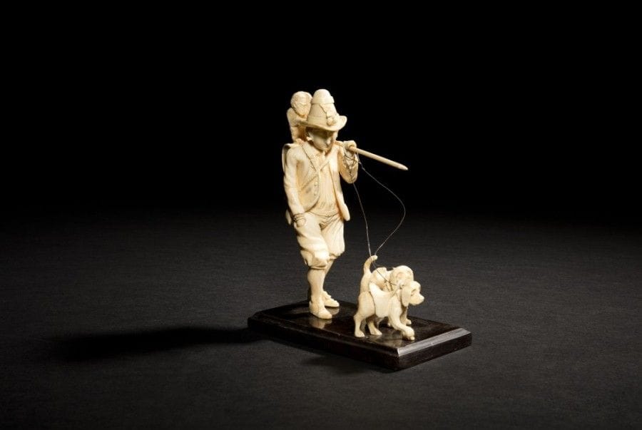 Le montreur d’animaux en ivoire sculpté en ronde-bosse. L’homme est représenté marchant, la main droite dans la poche de son pantalon ; il porte un bâton sur une épaule auquel est suspendu un tambour sur lequel se tient assis un singe ; il a un baluchon dans le dos et tient en laisse deux petits chiens ; sur un socle en bois noirci..
Dieppe, XIXe siècle.
Hauteur : 16 cm.

