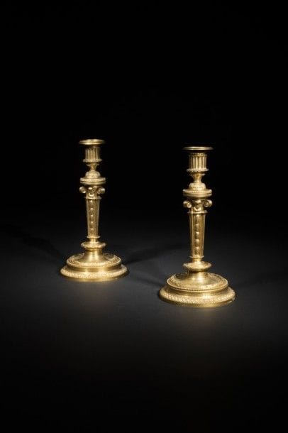 Paire de grands flambeaux en bronze doré, le fût à pans, brettés et chutes de feuillages, à chapiteaux ioniques, reposant sur une base circulaire à emmarchements à feuilles de laurier et rais de cœurs..
Époque Louis XVI.
H : 32,5 cm.
 