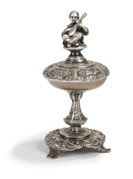 Auguste FANNIERE (1818 - 1900) et Joseph FANNIERE (1820 - 1897).
Rare sonnette de table en bronze argenté. Reposant sur une base tripode ciselée de volutes et d’une frise de grecques, le timbre est déclenché par une pression sur la prise figurant un chinois assis, les jambes croisées et jouant du luth, traité en ronde bosse..
Signé sous la base..
Il s’agit d’une rare représentation dans la production éclectique des deux frères. On retrouve dans le sujet tout le talent et le goût d’Auguste pour la sculpture ainsi que l’humour dont il faisait preuve dans le choix de ses modèles. A notre connaissance aucun autre exemplaire de ce type d’objet ne figure dans leurs deux ventes après décès ni dans la liste des oeuvres répertoriées à ce jour..
H :16 cm