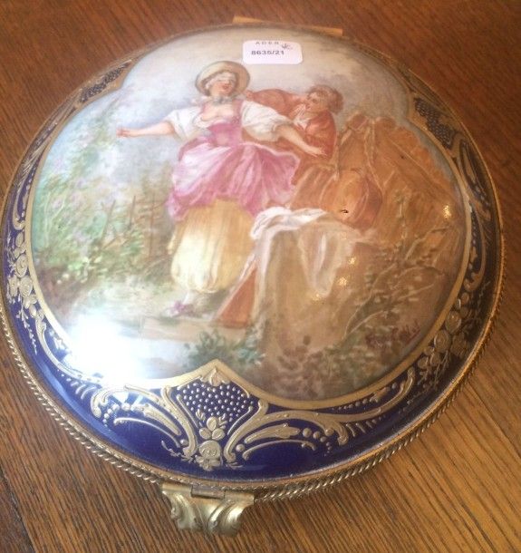 8635/21 Boîte circulaire en porcelaine à fond gros bleu et or à décor en polychromie d'une scène de jeu galant. Monture de bronze doré.
Sèvres vers 1900
(Hauteur :12,5 x Diamètre :18cm)