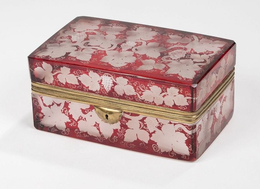 Coffret en verre gravé à décor de pampres de vigne sur fond teinté rouge, à bordure de laiton, ouvrant à charnières.
Fin du XIXe siècle.
H.: 9 cm, L.: 18,5 cm, P.: 11 cm