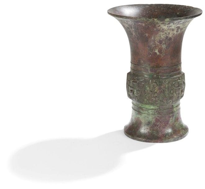 CHINE - Époque ZHOU 
Vase Zun en bronze à patine brune verdâtre à décor de masques de taotie en relief sur la panse. 
(Retaurations et manque). 
Hauteur : 25,3 cm