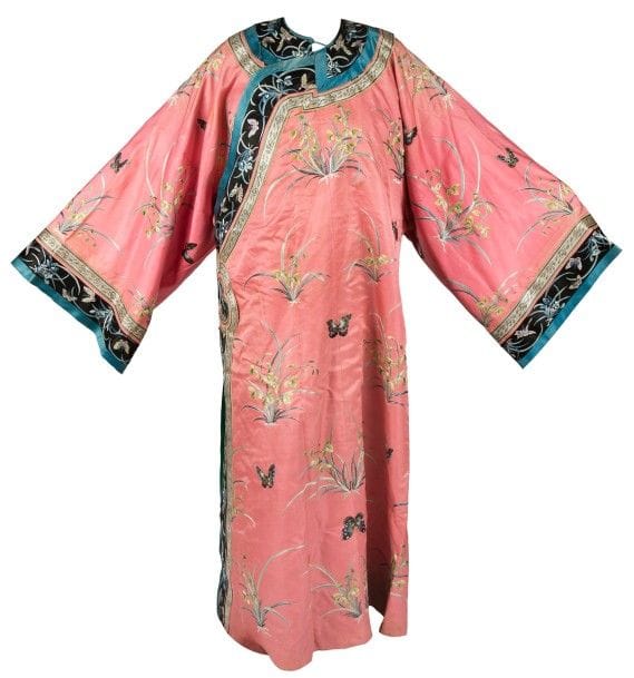 CHINE - Fin XIXe siècle
Robe de femme en soie rose à décor brodé de papillons et orchidées, doublée en soie verte. 
Hauteur : 125 cm