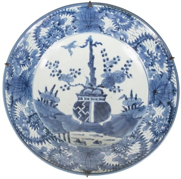 JAPON, Fours d’Arita - Époque EDO (1603 - 1868)
Grand plat rond en porcelaine à décor en bleu sous couverte d’un arbuste fleuri sur une terrasse, l’aile ornée de fleurs et de rinceaux. 
Diamètre : 44 cm