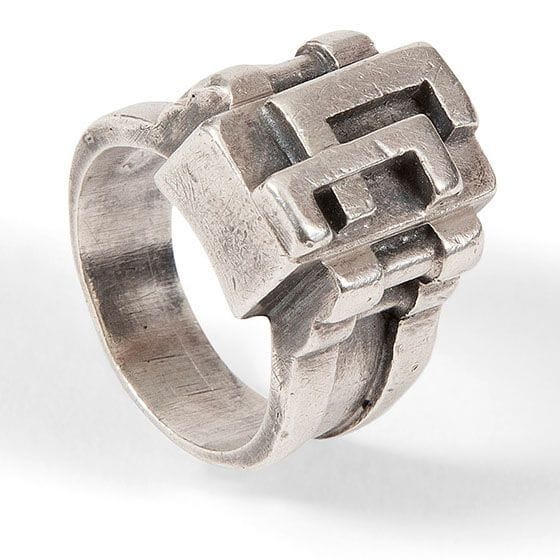 Jean DESPRÉS (1889-1980)
Rare bague moderniste en argent, les attaches traitées dans le goût des bijoux mécaniques dits Moteur.
L’anneau soutient, par un double agrafage latéral et cylindrique, la plateforme parallélépipédique au motif d’un monogramme stylisé.
Signée J. DESPRÉS à l’intérieur de l’anneau, porte les poinçons de Maître Orfèvre et de garantie sur l’anneau.
Poids : 11,75 g

Provenance :
Ancienne Collection M. & Mme C. (Avallon – France), œuvre acquise par ceux-ci directement auprès de l’artiste.