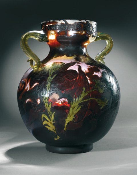 Émile GALLÉ (1846-1904) et Victor PROUVÉ (1858-1953).
Vase "Les hommes noirs, 1900", en verre soufflé de forme sphérique à col étranglé entre deux anses appliquées, décor floral dégagé à l'acide et repris à la roue, portant les inscriptions: "Hommes noirs, d'où sortez-vous ? / Nous sortons / de dessous terre / Béranger". Signé "Gallé 1900" et "V. Prouvé". Haut. : 39 cm. - Exposé à l'Exposition Universelle de Paris, 1900. - Présenté à l'exposition "L'Ecole de Nancy, 1889-1909", à Nancy, galeries Poirel, avril-juillet 1999, reproduit p.77 du catalogue. - Présenté à l'exposition "Le testament artistique d'Émile Gallé", à Paris, Musée d'Orsay, juin-septembre 2004, reproduit p. 133 du catalogue. - Exemplaire similaire au Musée de l'École de Nancy Historique : « La signification du vase "Hommes noirs d'où sortez-vous" est immédiate, non pas seulement par l'emprunt, alors pour tous évident, fait au pamphlet de Béranger, mais en raison de ses tonalités évocatrices des ténèbres. En cela, il s'inscrit dans la descendance de deux pièces antérieures d'une dizaine d'années, particulièrement remarquées pour leur coloration sombre. Sur la première, présentée à l'Exposition Universelle de 1889, un crapaud tapi dans l'ombre s'apprête à happer une libellule ; le second modèle montre un pélican aux prises avec un ptérodactyle. Le contraste entre la laideur repoussante des uns et la grâce aérienne des autres se veut symbole de la lutte des forces du bien et du mal. Lutte tout à fait apte à évoquer un combat politique contemporain, puisque l'un des exemplaires du vase au pélican fut en décembre 1890 dédicacé par Gallé à l'un des champions de l'émancipation irlandaise, William O'Brien. Les hommes noirs constituent à leur tour un bel exemple du rôle primordial des effets de matière dans le pouvoir de suggestion d'une oeuvre. Des janvier 1889, Gallé s'était adressé à Victor Prouvé, déjà sollicité en 1888 pour l'élaboration des oeuvres emblématiques faisant appel à la figure humaine. Durant une année entière, le peintre fait parvenir au verri