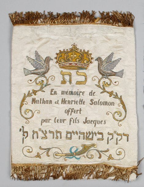 MANTEAU DE THORA - Velours blanc et broderie de fils de métal doré et argenté, avec une inscription à la mémoire de Nathan et Henriette Salomon en français (usures ; déchirure à la partie inférieure). Haut. : 51 cm - Larg. : 37 cm.