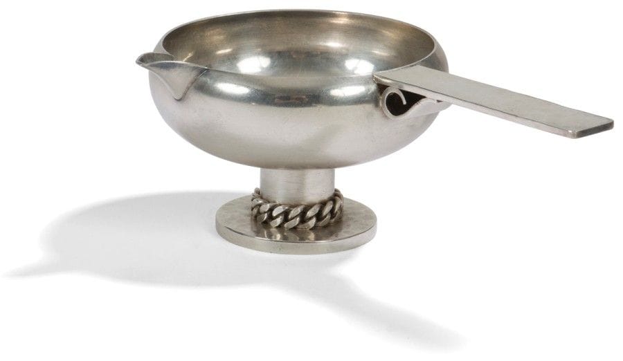 Jean DESPRÉS (1889-1980) 
Élégante saucière moderniste en métal argenté. Base circulaire martelée et ornée d’une gourmette à maillons plats. Prise plate et martelée fixée par une volute. Signée J. DESPRÉS à la pointe sous la prise. 7,7 x 21,5 x 14 cm 
(Provenance : Ancienne collection de Madame R. à Magny près d’Avallon, œuvre acquise directement auprès de l’artiste).