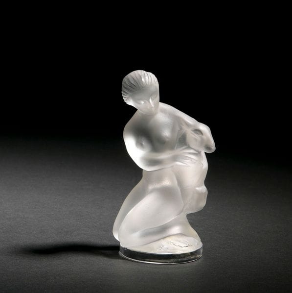 Maison LALIQUE 
Femme au chevreau 
Sujet décoratif. Épreuve en cristal moulé-pressé satiné. Un infime choc sur la tête de l’animal. Signé LALIQUE France en lettres cursives sous la base. 
H. : 11,5 cm 