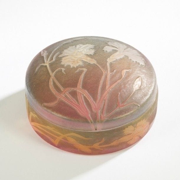 DAUM Nancy
Œillets du Japon
Bonbonnière circulaire. Épreuves, le dessus et la base, en verre blanc moulé, la base nuancée rose et jaune. Décor achevé en satiné sur fond granité et patiné gris. Signée DAUM Nancy à la Croix de Lorraine, gravé au revers de la base. 
H. : 7 cm - D. : 14,5 cm